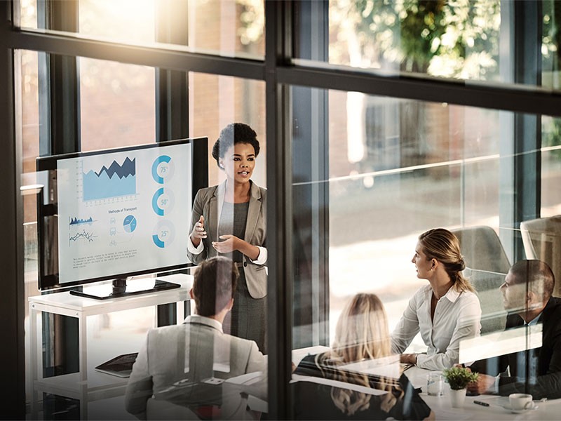 A woman is presenting to 4 other people in a conference room 